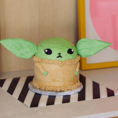 Baby Yoda Grogu cake with giant green chocolate ears and extra cute face sitting on a buffet