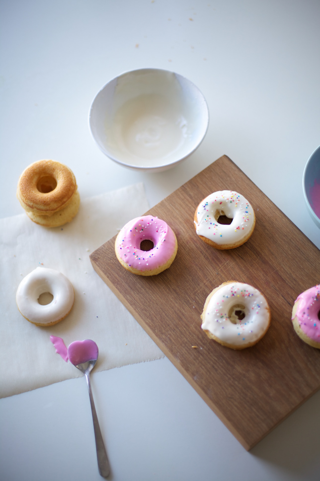 homemade doughnuts with icing and sprinkles on a wooden board and table