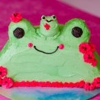 tiny buttercream frog sitting on top of buttercream frog cake with silly smiles