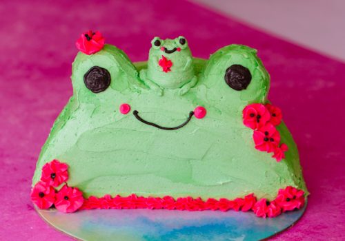 tiny buttercream frog sitting on top of buttercream frog cake with silly smiles