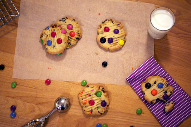 smartie cookies on table next to glass of milk