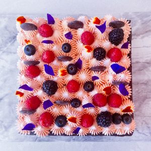 square chocolate cake with pink frosting and berries