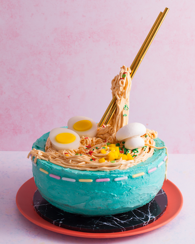buttercream ramen noodle cake in blue bowl with gold straws as chopsticks